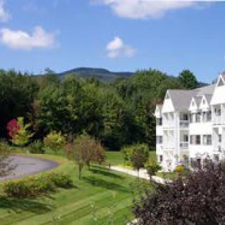 A scenic view of a white building surrounded by lush greenery, with mountains in the background.