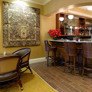A cozy bar interior with wooden chairs, a counter, and a decorative tapestry on the wall.