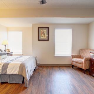 A cozy bedroom with wooden flooring, featuring a bed, armchair, and decorative elements.