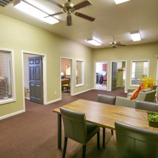 A spacious office interior with a large wooden dining table, chairs, ceiling fans, and multiple doorways.