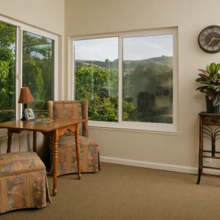 A cozy interior space with a desk and chairs overlooking a lush garden through the windows.