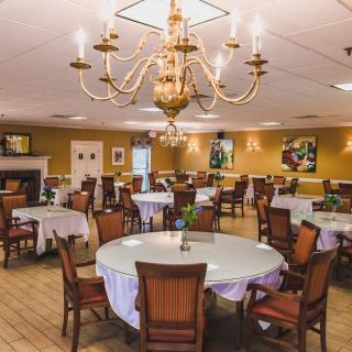 An elegant dining room with a central chandelier, round tables, and comfortable chairs.