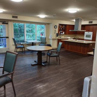 An open dining and kitchen area with wood flooring, featuring a table and chairs with large windows letting in natural light.