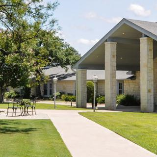 A modern building with a sloped roof and stone columns, surrounded by grassy areas and trees.