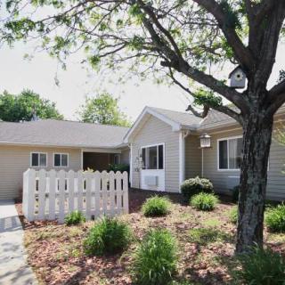 A charming suburban house with a white fence and landscaped front yard on a sunny day.