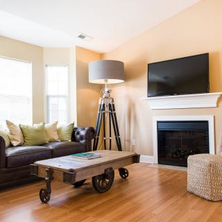 A cozy living room with a sofa, industrial-style coffee table, and a fireplace beneath a mounted television.