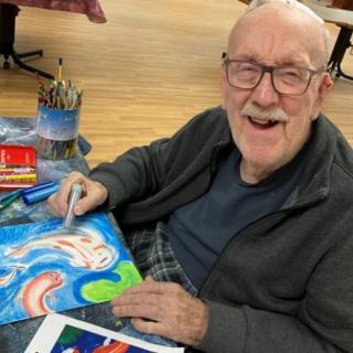 An elderly person happily creating a colorful painting indoors.