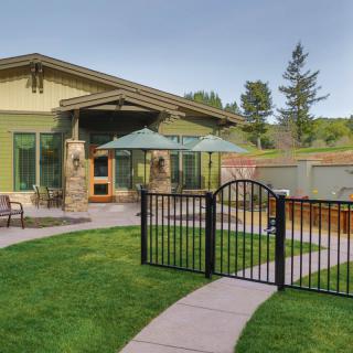 A modern patio and garden area with a small gate, lawn, and outdoor furniture.