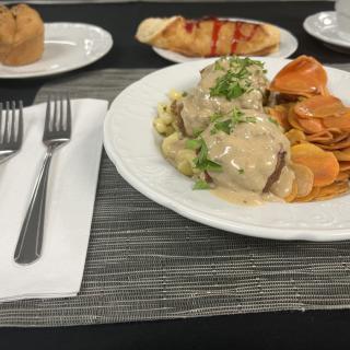 A plated meal consisting of meatballs with gravy and vegetables, accompanied by a bread roll and muffin.