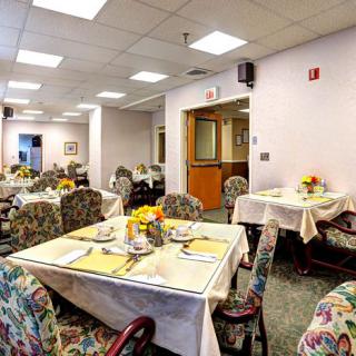 A well-lit dining room with tables set for a meal, featuring floral decorations and patterned chairs.