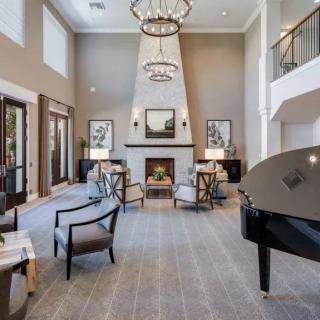A spacious and elegantly designed living room featuring a grand piano, fireplace, and high ceilings with chandeliers.