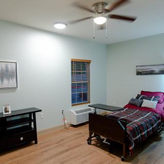 A simple bedroom with a hospital bed, featuring minimalist decor and wooden flooring.