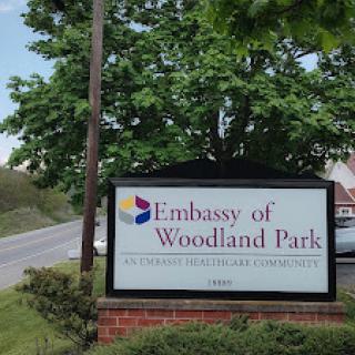 Signage for the Embassy of Woodland Park, surrounded by greenery.