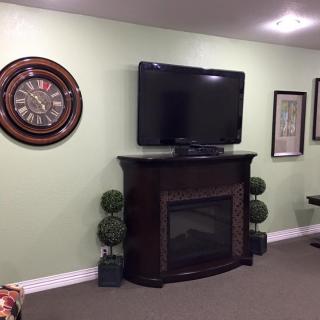 A cozy living room with a wall-mounted television above a fireplace, accompanied by a decorative clock and framed pictures.