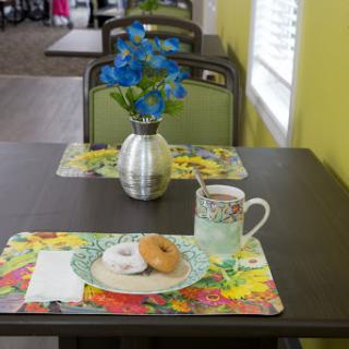 A cozy dining setup with a floral centerpiece, a cup of coffee, and a donut on vibrant placemats.