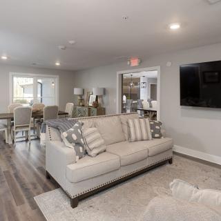 A modern and spacious living room with a comfortable sofa, dining area, and large wall-mounted television.