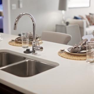 A modern kitchen sink with a chrome faucet and neatly set dining area on the countertop.