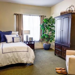 A cozy bedroom with a neatly made bed, a wooden wardrobe, and a potted plant by the window.