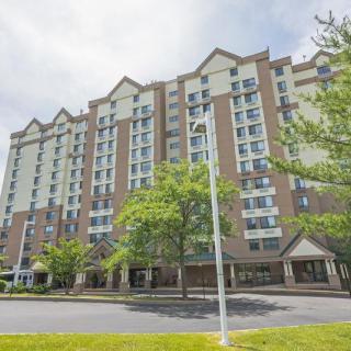 A multi-story residential apartment building with a landscaped entrance and trees in the foreground.
