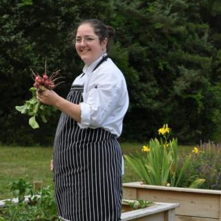 A chef in an apron holding freshly picked vegetables in a garden.