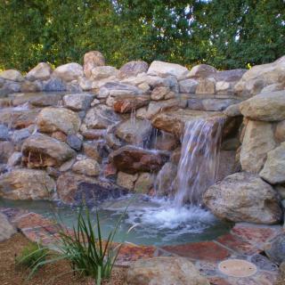 A serene garden waterfall cascading over natural rocks into a small pond.