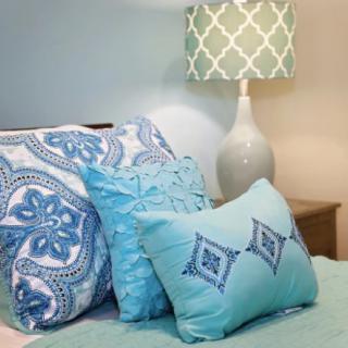 A cozy bedroom setup featuring blue decorative pillows and a patterned lamp.