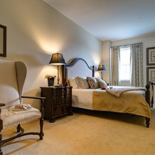 A cozy, elegantly decorated bedroom with a large bed, upholstered chair, and stylish lamps.