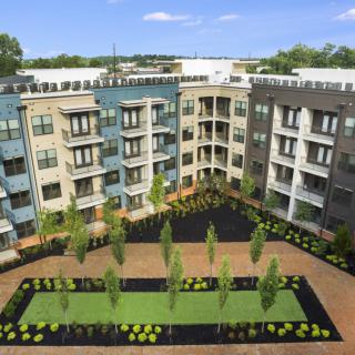 A modern apartment complex with a landscaped courtyard featuring green spaces and trees.