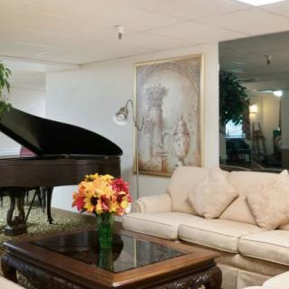 A cozy living room featuring a grand piano, comfortable sofa, and elegant decor with flowers and artwork.