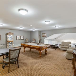 A spacious game room featuring a pool table, seating area, and warm lighting.