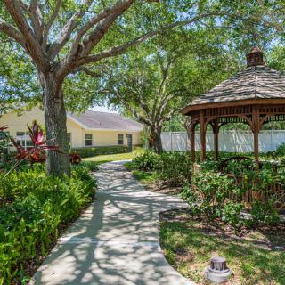 A serene garden pathway leading to a wooden gazebo, surrounded by lush greenery and trees.