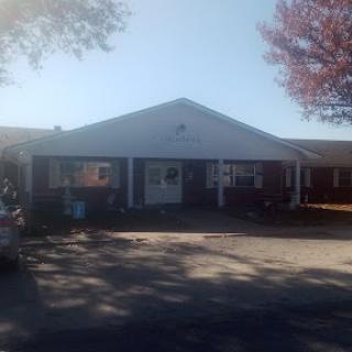 A view of a charming single-story building surrounded by trees and bathed in sunlight.