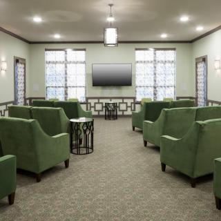 A modern lounge with green chairs and a television, featuring large windows and soft lighting.