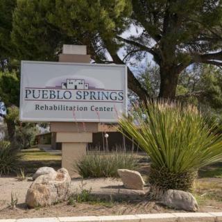 Sign for Pueblo Springs Rehabilitation Center surrounded by trees and plants.