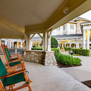 A spacious porch with wooden rocking chairs overlooking a landscaped garden and building.