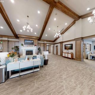 Spacious lobby with chandeliers and wooden ceiling beams, featuring decorative plants and a reception area.