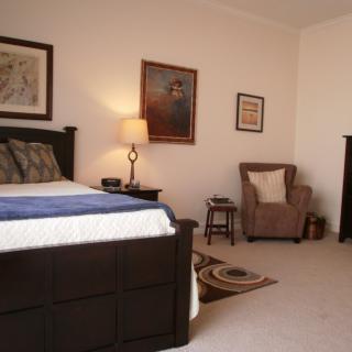 A cozy bedroom with a large bed, armchair, and wall art.
