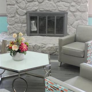 A cozy living room featuring a stone fireplace, armchairs, and a coffee table with a flower arrangement.