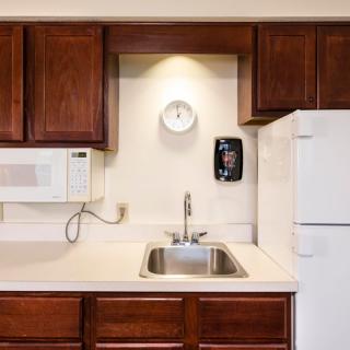 A compact kitchen with wooden cabinets, a sink, microwave, and refrigerator.