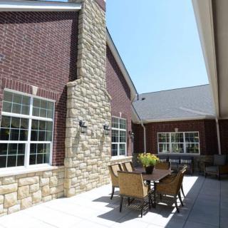 A patio area with a table and chairs set against a brick and stone building on a sunny day.