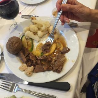 A plate of food featuring beef, vegetables, and a potato with a glass of red wine.