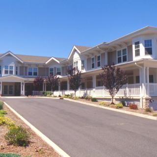 A large residential building with a driveway and landscaping under a clear blue sky.