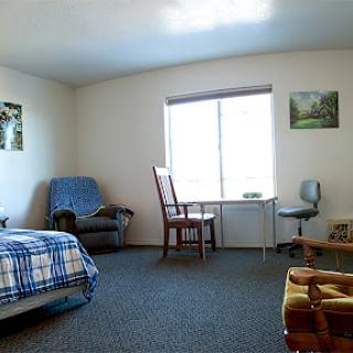 A simple and cozy room featuring basic furniture, a window for natural light, and decorative paintings.