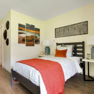 A modern bedroom with stylish decor and artwork, featuring a neatly made bed with vibrant pillows and a throw blanket.