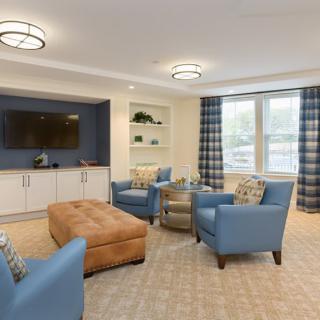 A modern living room with blue chairs, a brown ottoman, and a large television.