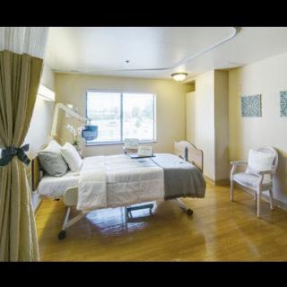 A clean and well-lit hospital room with a bed, chair, and window.