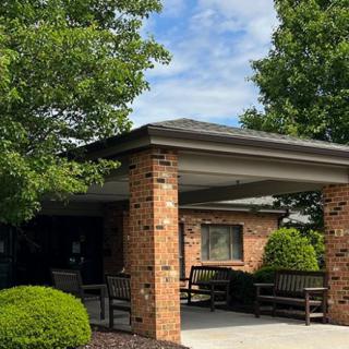 A brick building with a covered entrance, surrounded by lush greenery and benches.
