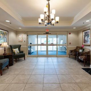 A spacious lobby with a chandelier, seating area, and tiled floor leading to glass double doors.