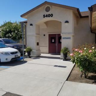 Entrance of a building with a parking lot and blooming flowers on a sunny day.