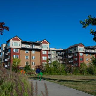 A modern apartment building surrounded by greenery and pathways under a clear blue sky.